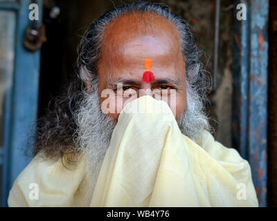 Lächelnde ältere Hindu Priester (pujari) deckt den unteren Teil seines Gesichtes mit seinem Gewand und seine Nase mit Gewand des Priesters blasen. Stockfoto