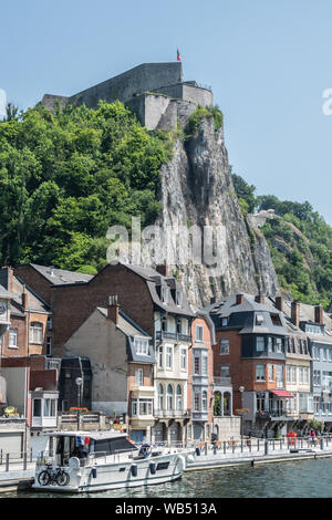 Dinant, Belgien - 26. Juni 2019: Von Norden der rechten Bank mit Unternehmen und Häuser gesehen, Citadelle vorne oben mit belgischer Flagge und Menschen. Stockfoto