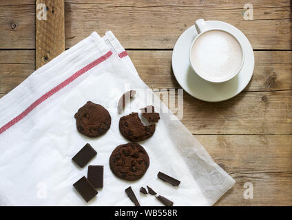 Schokolade Kekse, Schokolade und eine Tasse Kakao oder Kaffee mit Milch auf einem hölzernen Hintergrund. Im rustikalen Stil. Stockfoto