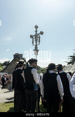 Zelebranten in traditioneller Kleidung tragen ein Prozessionskreuz während die Begnadigung von Feuer im Dorf St. Jean du Doigt, Bretagne, Frankreich. Eine Begnadigung ist ein typisch bretonische Form der Wallfahrt und eines der traditionsreichsten Demonstrationen der beliebten Katholizismus in der Bretagne. Stockfoto