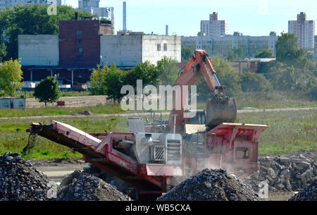 Schwere Bagger arbeiten im Steinbruch auf dem Hintergrund von Sonnenuntergang und blauer Himmel. Mobile kiefer Steinbrecher von der Baustelle. Crushing alte Beton wurde Stockfoto