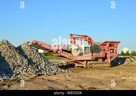 Schwere Bagger arbeiten im Steinbruch auf dem Hintergrund von Sonnenuntergang und blauer Himmel. Mobile kiefer Steinbrecher von der Baustelle. Crushing alte Beton wurde Stockfoto