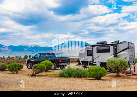 TAOS, NM, USA-4 JULI 2018: Eine Ram Pickup und einem Camplite RV Trailer in einer Wüste Campground geparkt, mit einem dunstigen Bergkette dahinter. Stockfoto