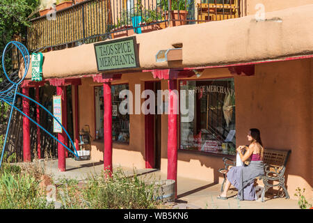 TAOS, NM, USA-8 JULI 2018: Eine attraktive Frau wartet im Halbschatten auf einer Bank in Taos Gewürzhändler, auf einem sonnigen Juli Tag. Stockfoto