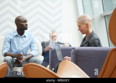 Seitenansicht Portrait von erfolgreichen Senior Geschäftsfrau mit Laptop während der Arbeit im Büro Halle, Platz kopieren Stockfoto