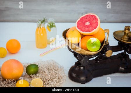 Frische Zitrusfrüchte in vintage Skala und einige Orangen, Zitronen, Grapefruit, Limette und hausgemachten Getränken auf die weiße Holztisch mit ein paar Gewichte. Uhr Stockfoto