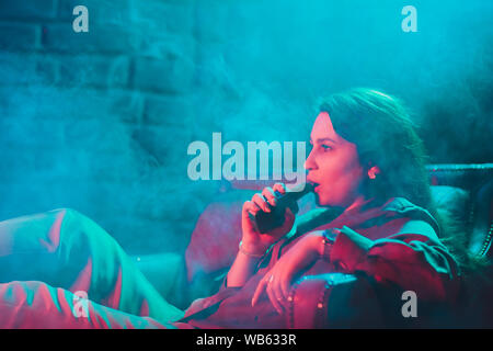 Frau raucht eine e-Zigarette liegen auf dem Bett im Zimmer. Raucher Konzept dampfen Stockfoto