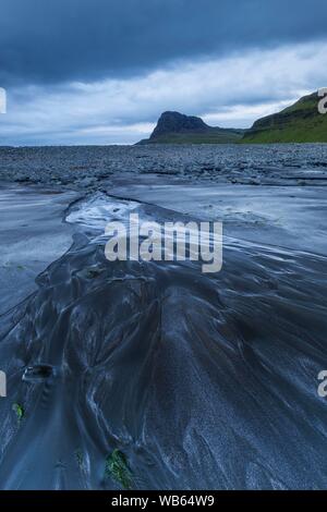 Kleiner Bach fließt in das Meer über einem schwarzen Sandstrand, Ebbe in Talisker Bay, Isle of Skye, Schottland Stockfoto