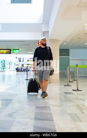 Junger Mann mit Hut gehen durch einen Flughafen Terminal mit einem Koffer Stockfoto