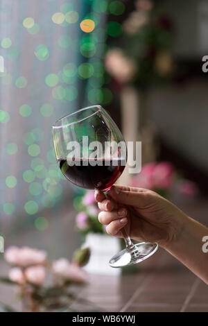 Hand sommelier Holding Glas Rotwein. Glas Rotwein auf dem Hintergrund der farbenfrohen Bar. Bokeh. Kalte Muskelaufbau. Platz für Text. Konzept alkoholisches Getränk Stockfoto