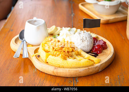 Süßes Wasser gießen auf die Waffeln mit Eis und Früchte wie Bananen, Kiwi und Erdbeeren in Holz- Platte auf dem Tisch. Stockfoto