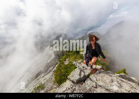 Abenteuerliche Mädchen ist Wandern auf einem steilen Weg nach oben einen schönen Rocky Mountain bei einem bewölkten Sommermorgen. Auf Crown Mountain, North Vancouver, BC genommen Stockfoto