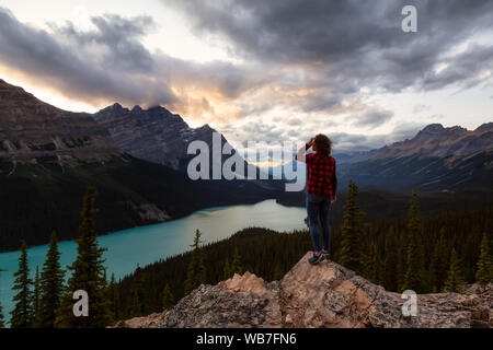 Abenteuerliche Mädchen stehen am Rand einer Klippe mit Blick auf den schönen kanadischen Rockies und Peyto Lake während einer lebhaften Sommer Sonnenuntergang. In Ba genommen Stockfoto