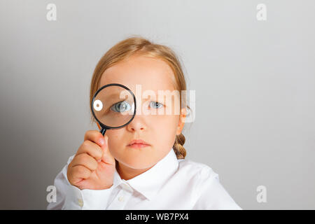 Kleines Mädchen sieht durch eine Lupe mit Interesse. Der Begriff der Bildung, Schule, Forschung, suchen. Stockfoto