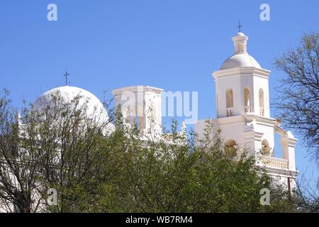 Die historische Mission San Xavier, die sich außerhalb von Tucson, Arizona, befindet, ist über das Frühlingslaub hinaus in Silhouette gegen einen klaren blauen Himmel zu sehen. Stockfoto