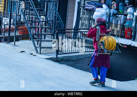 Shimla, Himachal Pradesh, Indien - 20. Juli 2019: Indische Frauen gehen auf die Straße. schweres Heben elektrische Kabel rollen auf den Kopf. Stockfoto