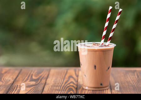 Eis Schokolade Milchshake in Einweg Plastikbecher mit waffelröllchen auf hölzernen Tisch im Freien Stockfoto