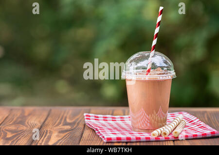 Eis Schokolade Milchshake in Einweg Plastikbecher mit waffelröllchen auf hölzernen Tisch im Freien Stockfoto