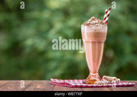 Schokolade Milchshake in Glas mit Schlagsahne und waffelröllchen auf hölzernen Tisch im Freien Stockfoto