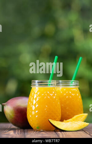 Frischen Mangosaft in zwei Gläser mit reifen Früchten auf hölzernen Tisch im Freien. Sommer erfrischendes Getränk Stockfoto