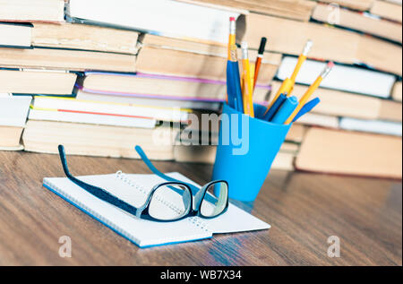 Stapel von alten Buch, Kugelschreiber und Bleistifte in Halter, geöffnet Notebook und Gläser. Bildung Konzept Hintergrund, viele Bücher Stapel mit Platz für Text kopieren Stockfoto