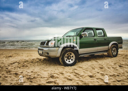 Grün Pick-up-Truck auf dem sandigen Strand mit Meer geparkter, blauer Himmel und Wolken im Hintergrund Stockfoto