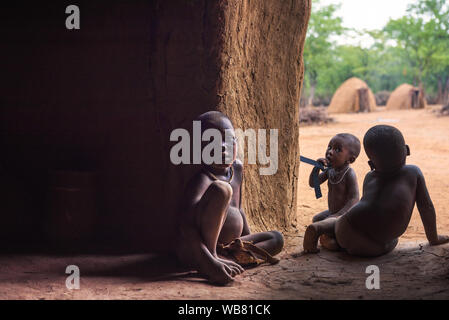 Drei Kinder der Himba in Namibia spielen in ihrer Hütte Stockfoto