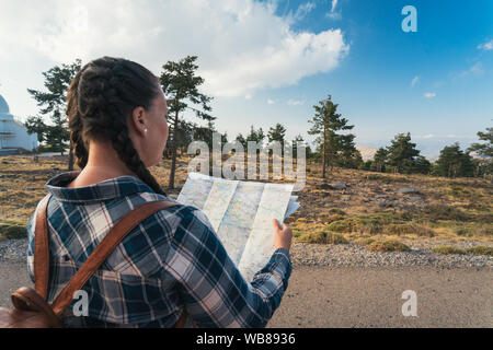 Junge Reisen Frau mit Zöpfen und Rucksack, stehend in der Wildnis mit Karte auf dem Berg. Stockfoto