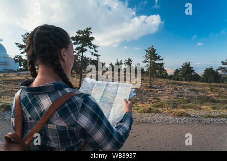 Junge Reisen Frau mit Zöpfen und Rucksack, stehend in der Wildnis mit Karte auf dem Berg. Stockfoto