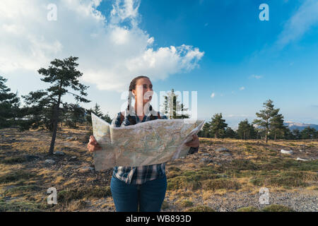 Junge Reisen Frau mit Zöpfen und Rucksack, stehend in der Wildnis mit Karte auf dem Berg. Stockfoto