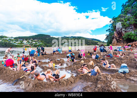 COROMANDEL, NEUSEELAND - Oktober 13, 2018: Touristen, graben Löcher in den Sand aus Vulkangestein an der Hot Water Beach Stockfoto