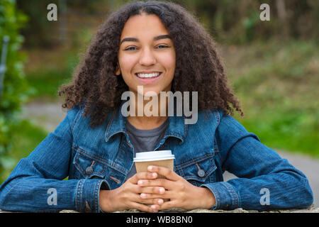Schöne happy biracial Mixed Race African American Girl Teenager weibliche junge Frau lächelnd mit perfekte Zähne trinken Kaffee zum Mitnehmen vor Verschleiß Stockfoto