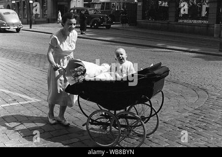 Mutter mit Kind in den 1950er Jahren. Sie geht in die Straße schieben Kinderwagen vor ihr, mit ihrem Baby. Schweden 1953. Kristoffersson Stockfoto