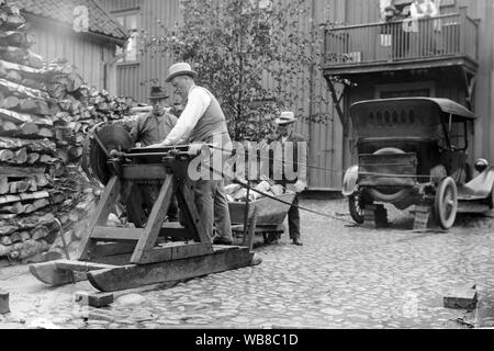Innovativ in den 1920er Jahren. Eine Gruppe von Männern sind Brennholz in der Straße. Sie verwenden das Hinterrad des Autos als Kraft an die Säge und einen Riemen die beiden anschließen. Eine innovative Lösung. Stockfoto