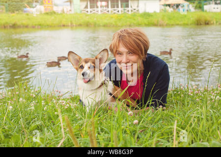 Ziemlich senior liegende Frau auf grünem Gras und Ihr corgi Hund umarmt Stockfoto