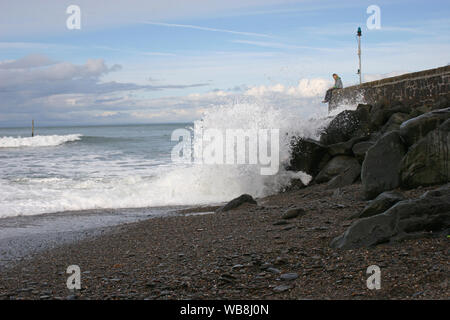 Ein paar sitzen auf der Kaimauer des Hafens arm in Lynmouth mit stürmischen Meer Wellen brechen an den Felsen unterhalb Stockfoto