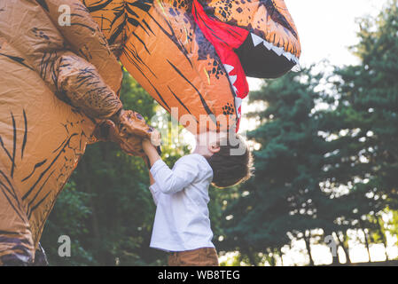 Vater und Sohn spielen im Park, mit einem Dinosaurier Kostüm, Spaß mit der Familie im Freien Stockfoto