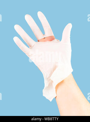 Gebrochen weißer latex Chirurg medizinische Handschuh auf kaukasische Hand auf Blau monocolor Hintergrund isoliert. Stockfoto