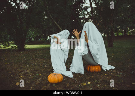 Vater und Sohn spielen Geister mit weißen Laken im Garten, konzeptionelle Fotos über Halloween Feiertage Stockfoto