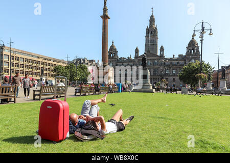 Glasgow, Schottland, Großbritannien. 25. August 2019. Da die Temperaturen in Glasgow über 26 C steigen nach Tagen der Regen und Kälte, Wind, Menschen strömen auf Freiflächen der Stadt George Square und den Botanischen Garten Vorteil der späten Sommer Sonne zu nehmen auf dieser August Bank Holiday, ihre Bräune nach oben und zu entspannen. Credit: Findlay/Alamy leben Nachrichten Stockfoto