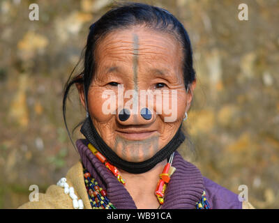 Alte Apatani tribal Frau mit schwarzem Holz- nase Stopfen (yaping hullo) und unverwechselbares Gesicht Tribal Tattoo posiert für die Kamera. Stockfoto