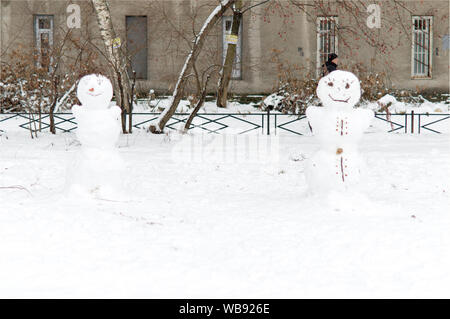 Fröhliche Schneemänner aus dem Schnee stehen im Hof eines Hauses in der Stadt und Lächeln. Stockfoto