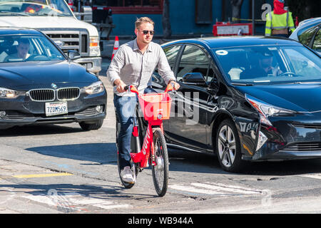 August 21, 2019 San Francisco/CA/USA - Mann, ein Sprung Elektrofahrrad; auf der rechten Seite ein Auto mit dem UBER Aufkleber gesehen werden kann; JUMP ist ein dockless Stockfoto