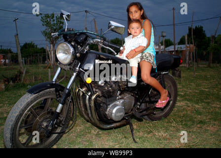 Am Ende des Tages mit einem bewölkten Himmel ein junges Mädchen und ein Junge auf einem großen schwarzen Motorrad in einer armen Gegend von Buenos Aires, Argentinien Stockfoto