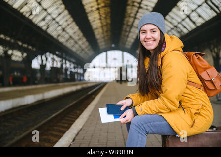 Junge hübsche Frau warten auf Zug am Bahnhof. Auf Taschen sitzen beim Warten auf die Bahn Stockfoto