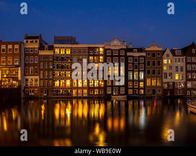 Historische Gebäude am Damrak Kanal in der Mitte des wunderschönen Amsterdam bei Nacht. Stockfoto