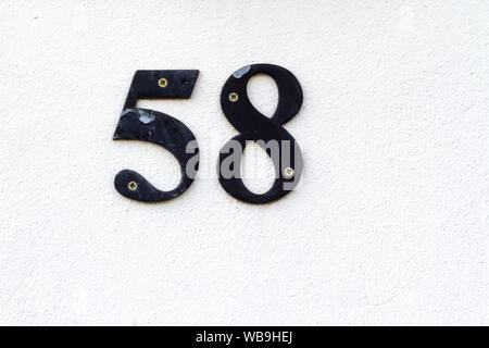 Haus Nummer 58 aus Metall in schwarz auf weißem Gips an der Wand Stockfoto