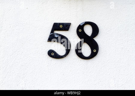 Haus Nummer 58 aus Metall in schwarz auf weißem Gips an der Wand Stockfoto