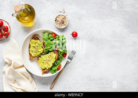 Avocado Toast serviert mit frischem grünen Salat von Kale, Olivenöl und Tomaten. Vegane, vegetarische Kost. Grauer Beton Hintergrund, Tischplatte ansehen und kopieren Stockfoto