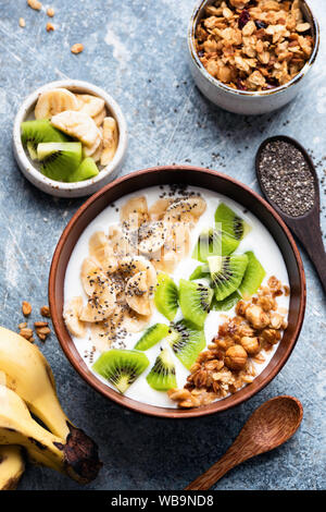 Frühstück Joghurt Schale mit Früchten, Müsli, Chia Samen. Tabelle Ansicht von oben. Griechischer Joghurt mit Kiwi, Banane, crunchy Hafer Honig Müsli Stockfoto